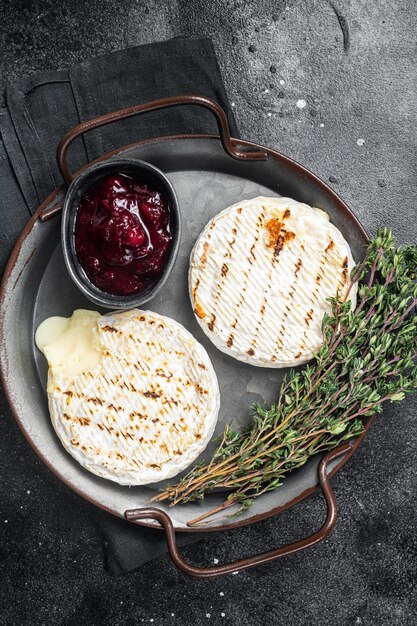 Camembert al forno su un vassoio d'acciaio con salsa di mirtilli rossi e timo Sfondo nero Vista dall'alto