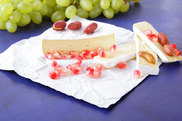 Camembert con semi di melograno uva verde e noci su sfondo blu Delizioso formaggio su carta pergamena da vicino