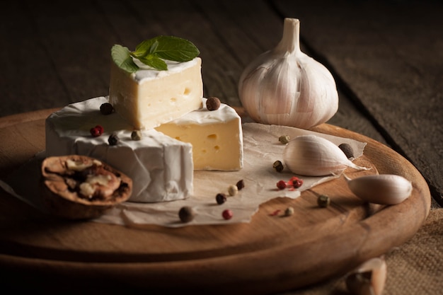 Camembert e brie su fondo di legno con pomodori, lattuga e aglio. Cibo italiano. Latticini.