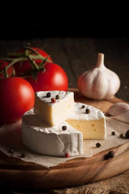 Camembert e brie su fondo di legno con pomodori, lattuga e aglio. Cibo italiano. Latticini.