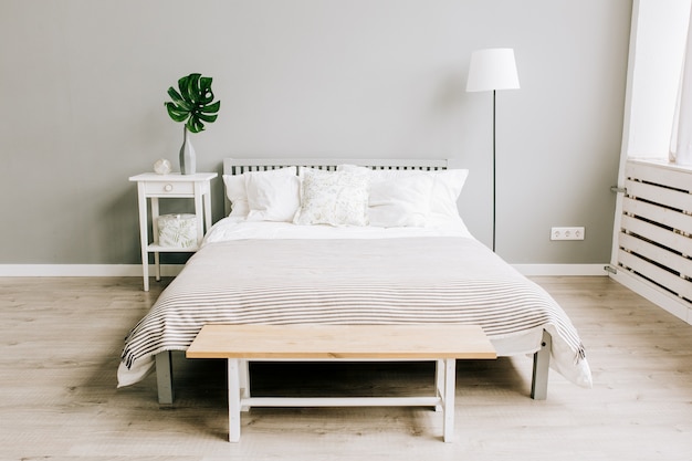 Camera da letto con mobili in legno in stile scandinavo e pianta monstera su un comodino di tronco d'albero