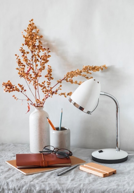 Camera luminosa e accogliente in stile scandinavo Un tavolo con una lampada da tavolo fiori in un vaso di ceramica disegna a matita un taccuino in pelle e occhiali