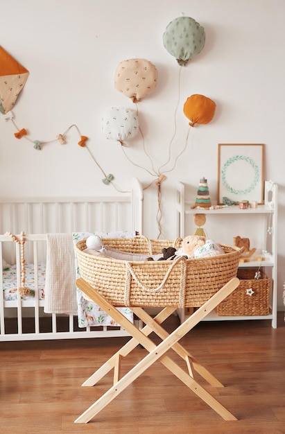 Camera per bambini, camera da letto, asilo nido in stile scandinavo bianco. Lettino con baldacchino. Scaffali e giocattoli in legno. Culla in vimini con gambe. Aquilone tessile e palloncini.