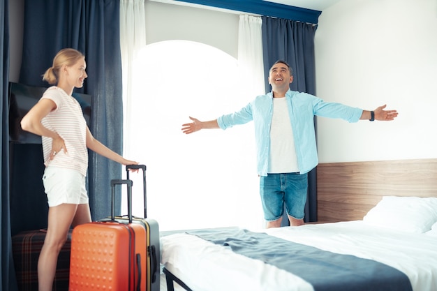 Camera spaziosa. Marito e moglie allegri in piedi in una stanza d'albergo con le loro valigie da viaggio disimballate felici di essere in vacanza.