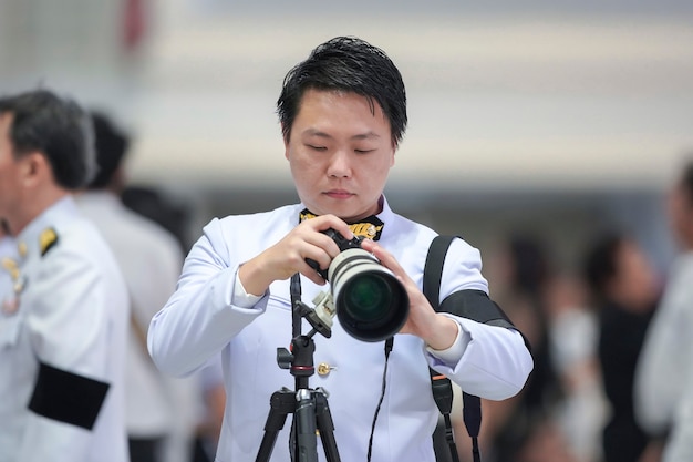 Cameraman professionista che tiene la fotocamera mirrorless con teleobiettivo davanti a sfocatura dello sfondo della folla.