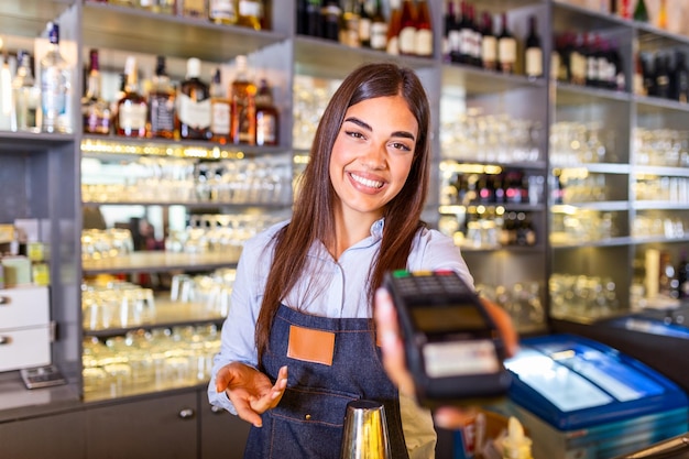 Cameriera al bancone che tiene una macchina per il pagamento con carta elettronica Close up di una giovane donna che tiene un terminale POS wireless in un caffè