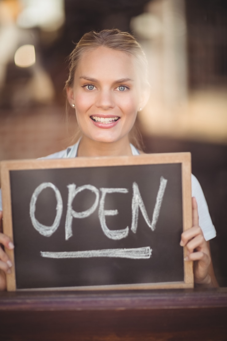 Foto cameriera bionda sorridente che mostra lavagna con il segno aperto