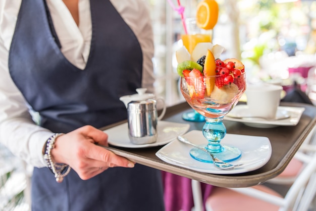 Cameriera che serve dessert di frutta e un drink