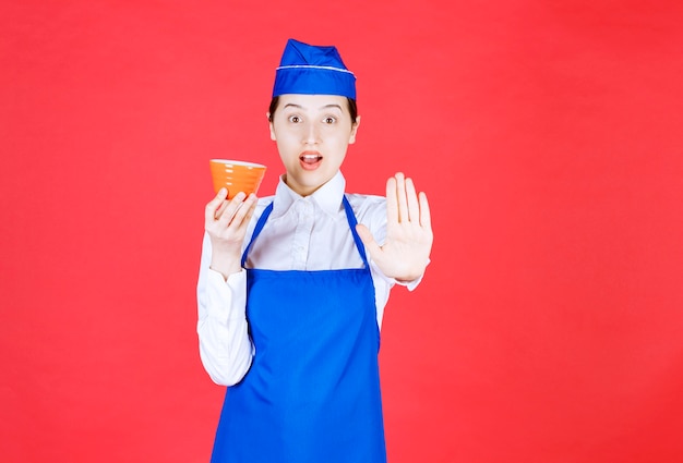 Cameriera della donna in uniforme che tiene una ciotola arancione e che fa il gesto di arresto.