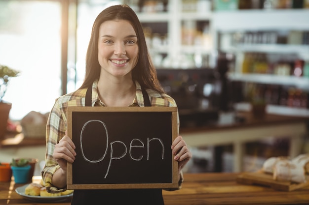 Cameriera di bar sorridente che mostra lavagna con il segno aperto