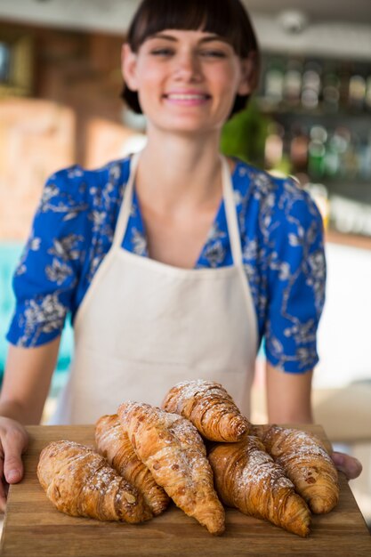 Cameriera di bar sorridente che tiene un vassoio di croissant