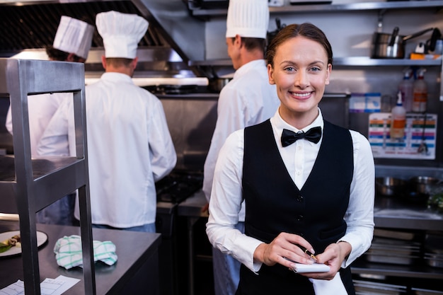 Cameriera di bar sorridente con il blocco note in cucina commerciale