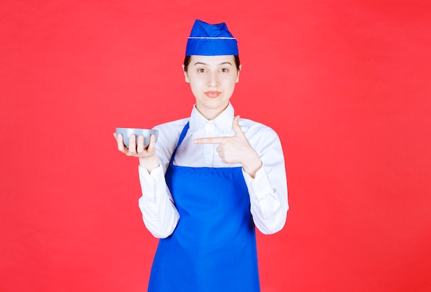 Cameriera donna in uniforme in piedi e indicando una ciotola sul muro rosso.