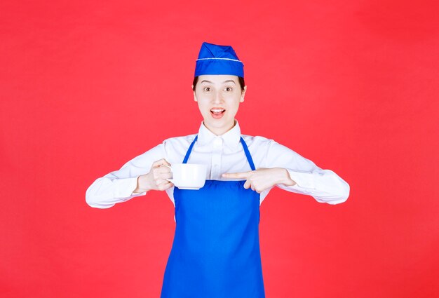 Cameriera donna in uniforme in piedi e indicando una tazza sul muro rosso.