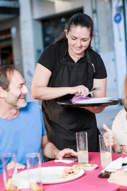 Cameriera latina donna sorridente che serve cibo nel ristorante a un gruppo maturo di amici insieme