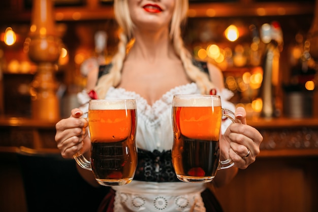 Cameriera sexy tiene due boccali di birra fresca nel pub.