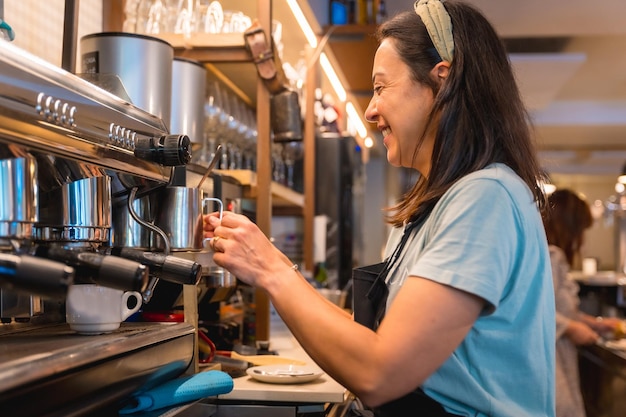 Cameriera sorridente in caffetteria che prepara il caffè nella macchinetta del caffè tolte le restrizioni dovute al covid e tolto l'uso obbligatorio delle mascherine