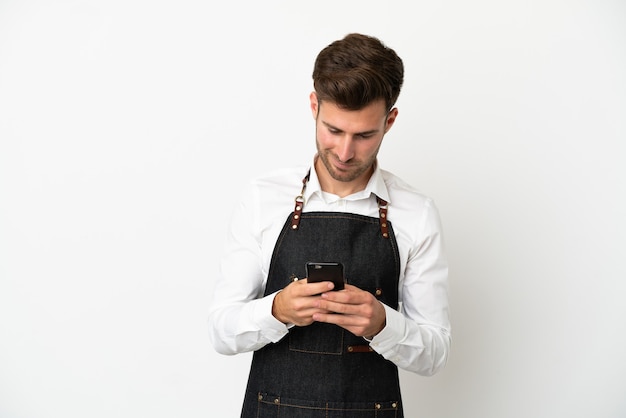 Cameriere caucasico del ristorante isolato su sfondo bianco che invia un messaggio con il cellulare