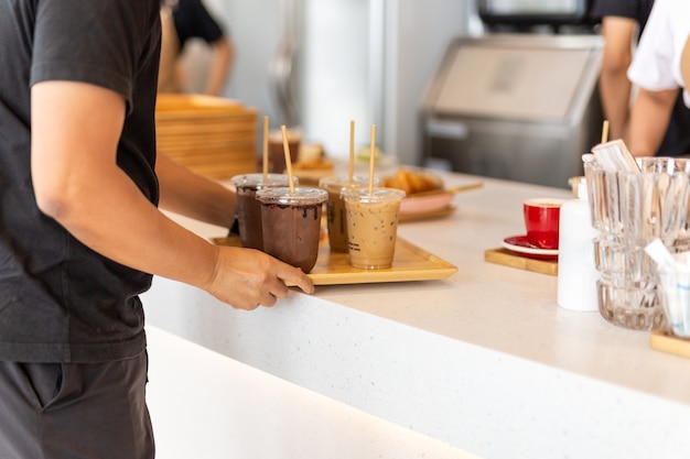 Cameriere che serve caffè freddo e cioccolato ghiacciato sul vassoio di legno al cliente