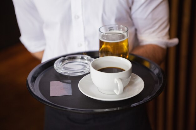 Cameriere che tiene vassoio con tazza di caffè e pinta di birra