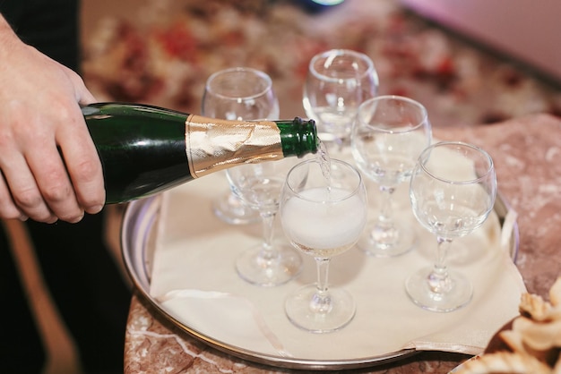 Cameriere che versa champagne in bicchieri vuoti al ricevimento di nozze celebrazioni di vacanze catering di lusso nel ristorante