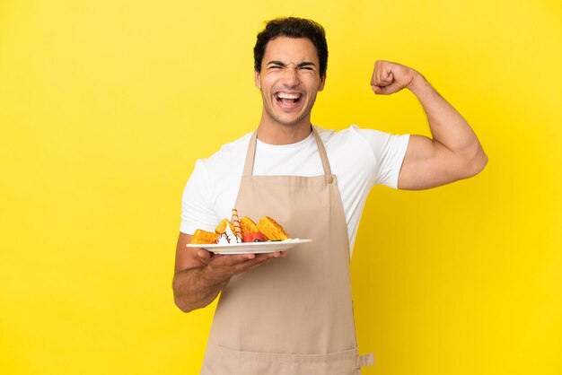 Cameriere del ristorante che tiene i waffle su sfondo giallo isolato facendo un gesto forte