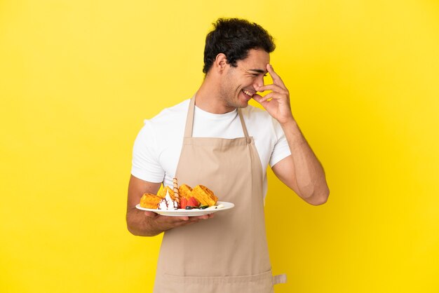 Cameriere del ristorante che tiene waffle su sfondo giallo isolato ridendo