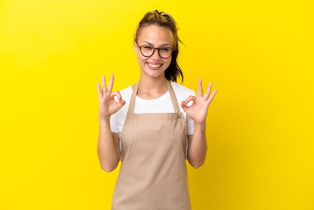 Cameriere del ristorante Ragazza russa isolata su sfondo giallo che mostra un segno ok con le dita