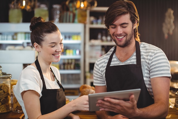 Cameriere e cameriera di bar sorridenti che per mezzo della compressa digitale al contatore