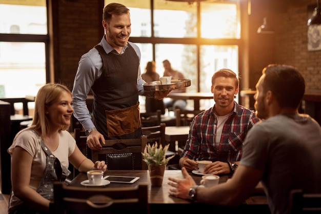 Cameriere felice che comunica con i clienti mentre porta loro i loro ordini in un bar