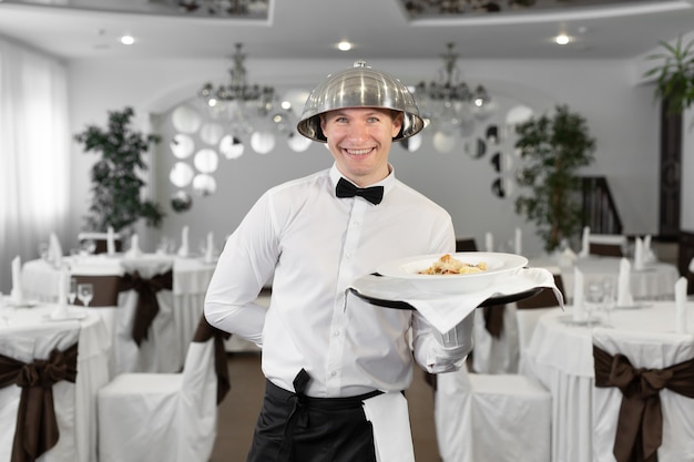 Cameriere maschio con un coperchio del vassoio sulla sua testa in un ristorante.
