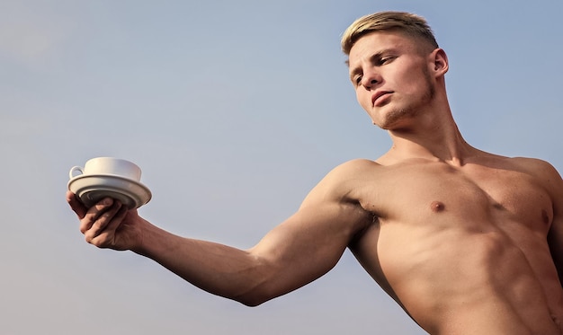 Cameriere petto nudo tenere tazza di caffè Sexy torso attraente cameriere Uomo muscoloso atleta bodybuilder ti offre caffè Macho petto muscoloso torso nudo tenere tazza di caffè fresco sfondo blu cielo