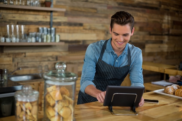 Cameriere sorridente che sta al contatore facendo uso della compressa digitale