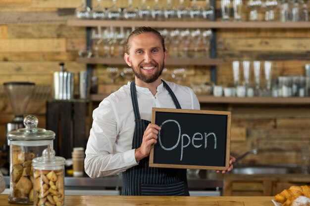 Cameriere sorridente che sta con il bordo aperto del segno in caffè