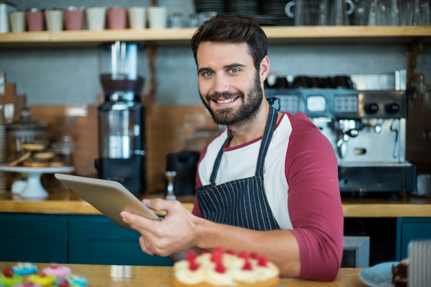 Cameriere sorridente che utilizza compressa digitale al contatore nel caffè