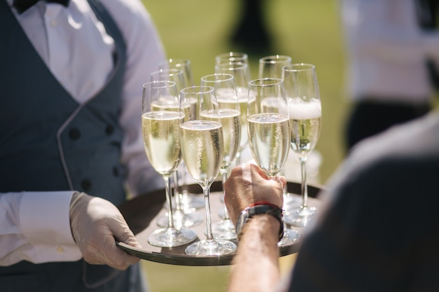 Cameriere tenere bicchieri di champagne sul vassoio all'aperto