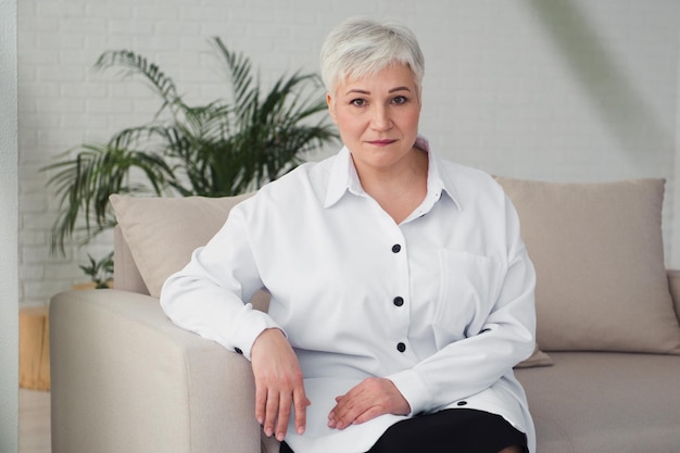 Camicia bianca donna dai capelli grigi seduta sul divano