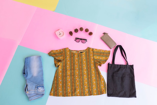 Camicia da donna, jeans blu, borsa marrone e borsetta nera su sfondo pastello multicolore. concetto di sfondo di moda