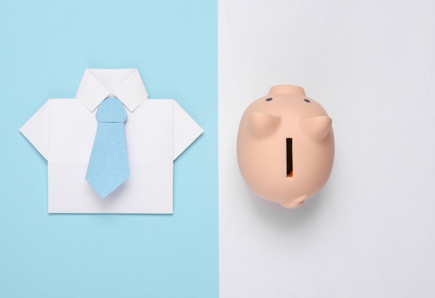 Camicia di carta origami con cravatta salvadanaio su sfondo bianco blu Concetto di economia, affari e finanza