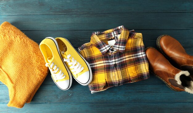 Camicia, maglione, scarpe da ginnastica e stivali sul tavolo di legno.