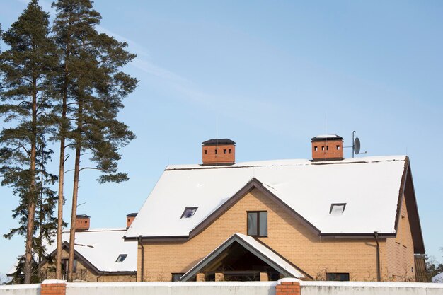 Camini di mattoni riscaldavano il cottage contro un cielo blu il tetto innevato del cottage