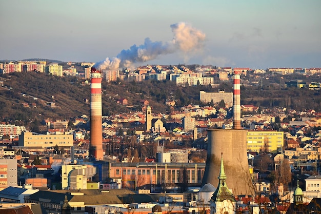 Camini fumanti con case in città Concetto per l'ambiente e l'industria Sfondo con il paesaggio della città al tramonto Brno Repubblica Ceca Europa