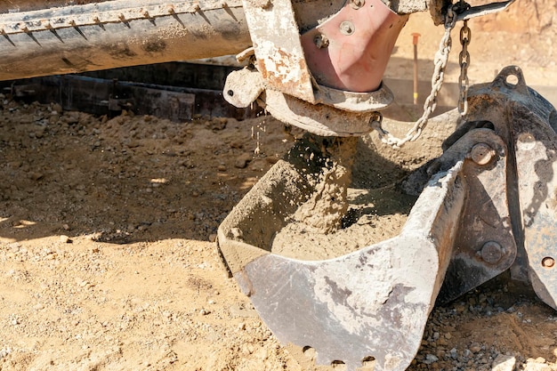 Camion betoniera che versa calcestruzzo fresco e umido nella benna degli escavatori in un cantiere