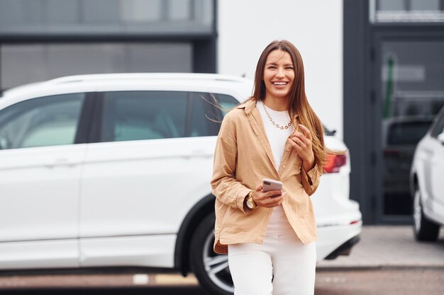 Cammina nelle vicinanze dell'auto Bella giovane donna alla moda e la sua automobile moderna