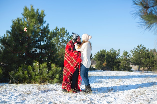 Camminando in inverno nei boschi un ragazzo avvolge la sua ragazza in un caldo plaid a scacchi rossi in modo che si riscaldi