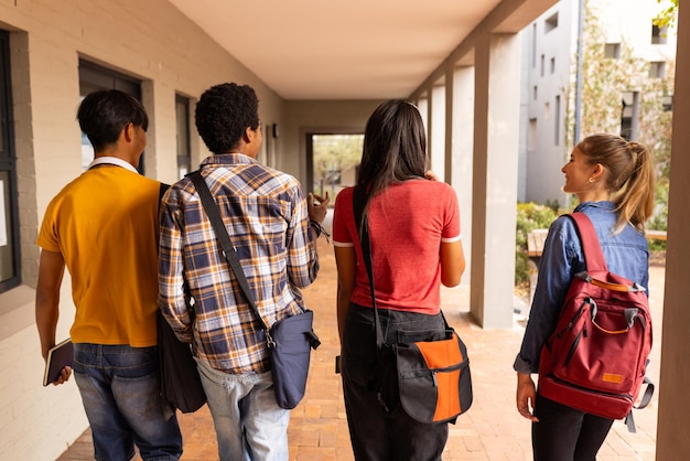 Camminando insieme con gli zaini, gli adolescenti chiacchierano fuori dall'edificio del liceo.