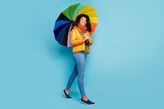 Camminata della signora della pelle scura con l'ombrello di colore dell'arcobaleno su fondo blu