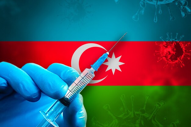 Campagna di vaccinazione dell'Azerbaigian Covid19 La mano in un guanto di gomma blu tiene la siringa davanti alla bandiera