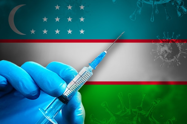 Campagna di vaccinazione dell'Uzbekistan Covid19 La mano in un guanto di gomma blu tiene la siringa davanti alla bandiera