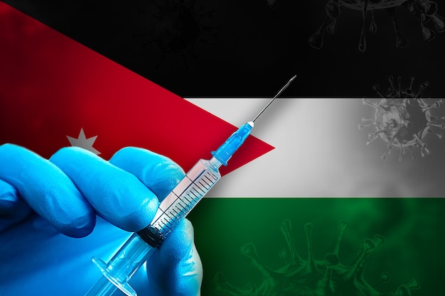 Campagna di vaccinazione Jordan Covid19 La mano in un guanto di gomma blu tiene la siringa davanti alla bandiera